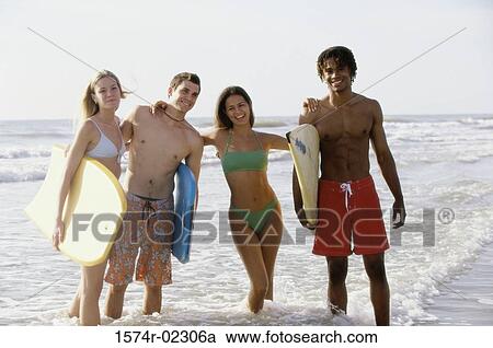 Stock Image - Portrait of two teenage couples standing on the beach holding boogie boards. Fotosearch