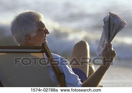 Rear view of a senior man reading a newspaper on the beach View Large Photo Image Stock Image - Rear view of a senior man reading a newspaper on the beach. Fotosearch