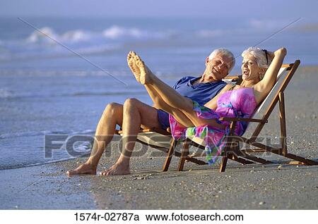 Stock Image - Senior couple sitting in deck chairs on the beach. Fotosearch