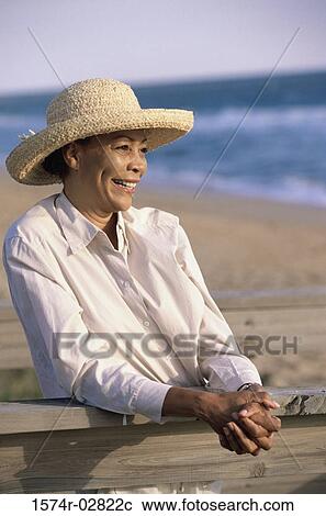 Stock Image - Senior woman standing on the beach. Fotosearch