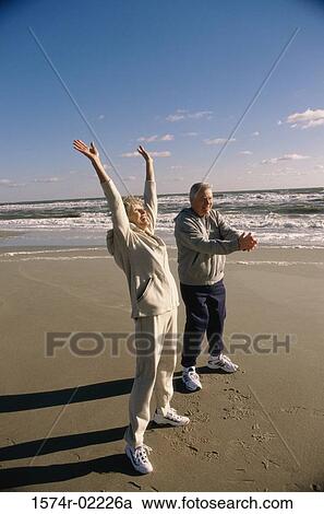 Stock Image - Side profile of a senior couple exercising on the beach. Fotosearch