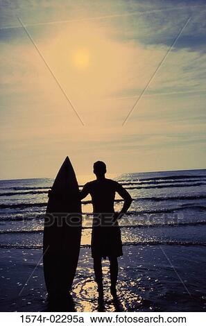 Silhouette of a man holding a surfboard standing on the beach View Large Photo Image Stock Image - Silhouette of a man holding a surfboard standing on the beach. Fotosearch