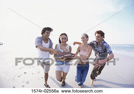 Stock Image - Two teenage couples playing football on the beach. Fotosearch