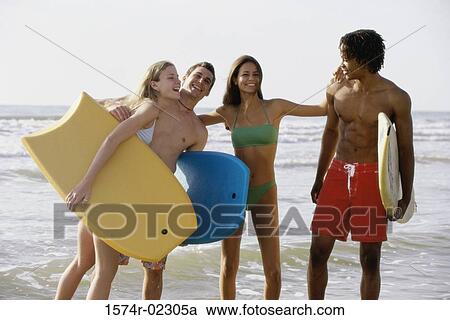 Two teenage couples standing on the beach holding boogie boards View Large Photo Image Stock Image - Two teenage couples standing on the beach holding boogie boards. Fotosearch