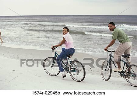 Stock Image - Young couple cycling on the beach. Fotosearch