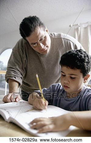 Boy writing in a book with his father standing beside him View Large Photo Image Stock Image - Boy writing in a book with his father standing beside him. Fotosearch