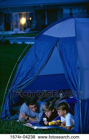 Stock Photo - Father with his two sons lying in a tent reading a book. Fotosearch