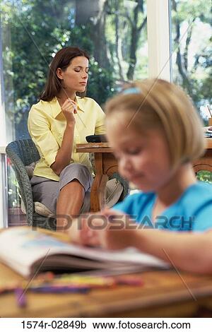 Stock Image - Girl writing in a book with her mother sitting behind her. Fotosearch