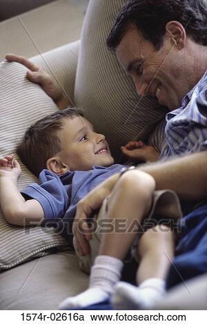 High angle view of a boy lying on a couch smiling with his father View Large Photo Image Stock Image - High angle view of a boy lying on a couch smiling with his father. Fotosearch