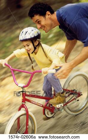 Stock Image - High angle view of a father teaching his daughter cycling. Fotosearch