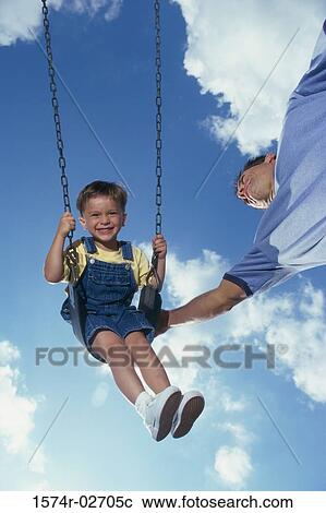 Stock Image - Low angle view of a father pushing his son on a swing. Fotosearch