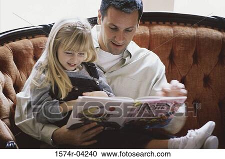 Stock Image - Man sitting on a couch with his daughter reading a book. Fotosearch