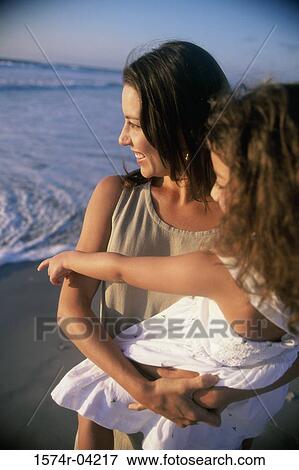 Stock Photo - Mother holding her daughter standing on the beach. Fotosearch