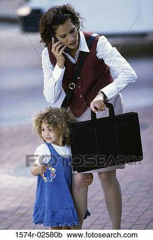 Mother talking on a mobile phone with her daughter standing beside her View Large Photo Image Stock Image - Mother talking on a mobile phone with her daughter standing beside her. Fotosearch
