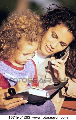 Stock Image - Mother talking on a mobile phone with her daughter standing beside her. Fotosearch