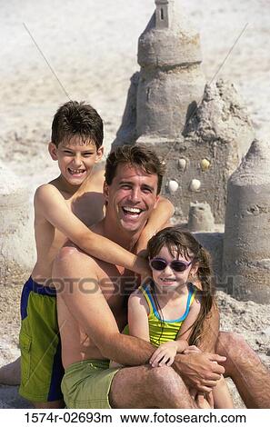Picture - Portrait of a father with his son and daughter sitting on the beach. Fotosearch