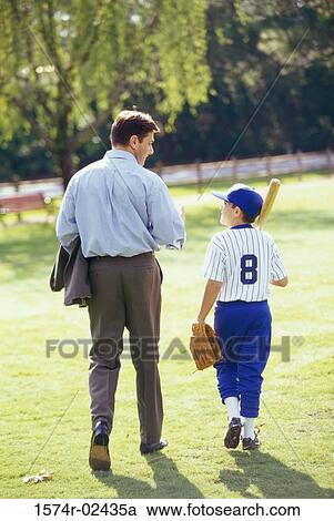 Stock Image - Rear view of a boy wearing a baseball uniform talking to his father. Fotosearch