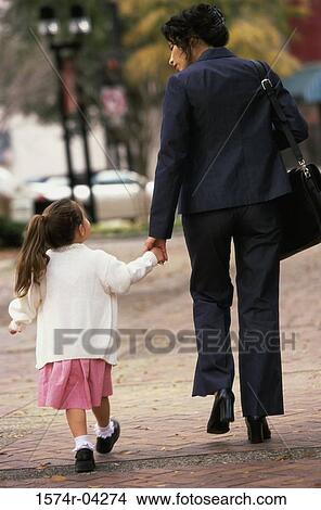 Rear view of a mother holding hands while walking with her daughter View Large Photo Image Picture - Rear view of a mother holding hands while walking with her daughter. Fotosearch