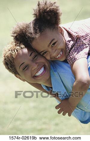Stock Image - Side profile of a daughter riding piggyback on her mother. Fotosearch