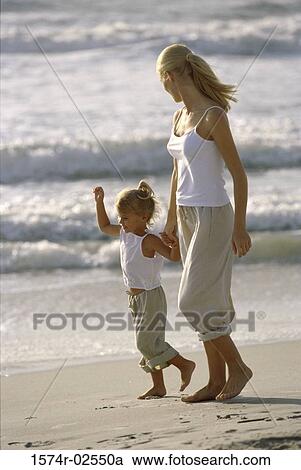 Stock Image - Side profile of a mother and her daughter walking on the beach. Fotosearch