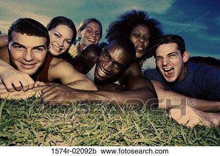 Stock Image - Portrait of a group of young men and women lying on grass. Fotosearch