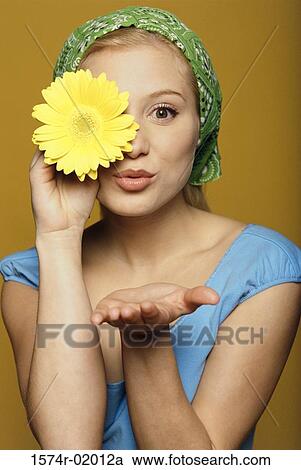 Stock Image - Portrait of a young woman holding a flower in front of her eye. Fotosearch