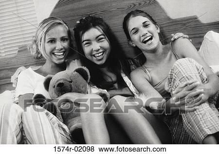 Stock Photo - Portrait of three teenage girls sitting on a bed at a slumber party. Fotosearch