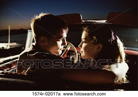 Stock Image - Rear view of a young couple sitting in a convertible car. Fotosearch
