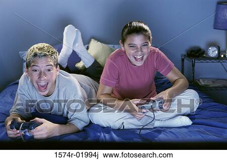 Teenage boy and girl sitting on the bed and playing a video game View Large Photo Image Stock Image - Teenage boy and girl sitting on the bed and playing a video game. Fotosearch