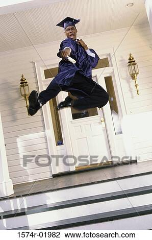 Stock Image - Teenage boy in a graduation outfit leaping on the porch. Fotosearch