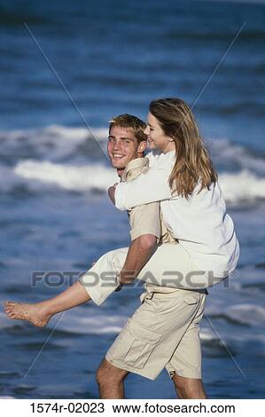 Teenage girl riding piggyback on a teenage boy at the beach View Large Photo Image Stock Image - Teenage girl riding piggyback on a teenage boy at the beach. Fotosearch