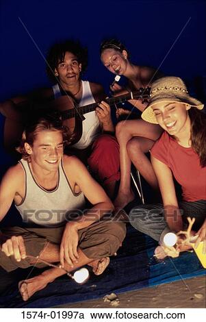 Stock Image - Two young couples sitting by a bonfire on the beach. Fotosearch