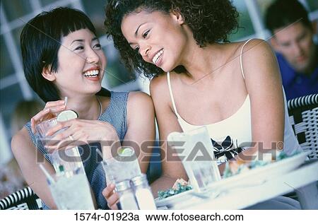 Two young woman seated at a table smiling View Large Photo Image Stock Image - Two young woman seated at a table smiling. Fotosearch
