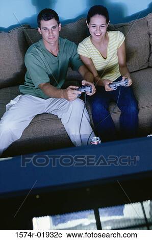 Stock Image - Young couple sitting on a couch and playing a video game together. Fotosearch