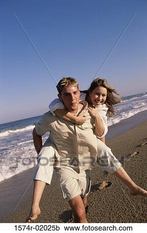 Young woman riding piggyback on a young man at the beach View Large Photo Image Stock Image - Young woman riding piggyback on a young man at the beach. Fotosearch