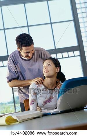 Young woman sitting in front of a laptop with a man behind her View Large Photo Image Stock Photograph - Young woman sitting in front of a laptop with a man behind her. Fotosearch