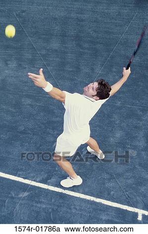 Stock Image - High angle view of man serving a tennis ball. Fotosearch