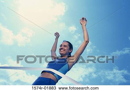 Stock Image - Low angle view of a female athlete crossing the finishing line. Fotosearch