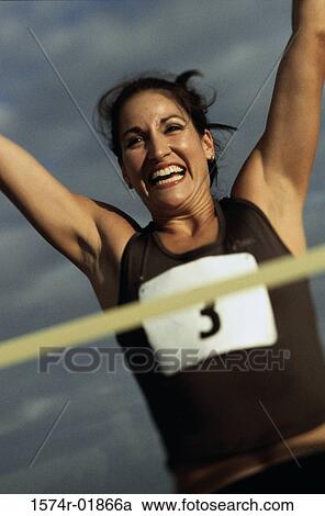 Stock Image - Low angle view of a female athlete with arms raised. Fotosearch