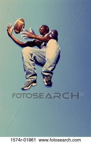 Stock Image - Low angle view of a man catching a football in mid-air. Fotosearch