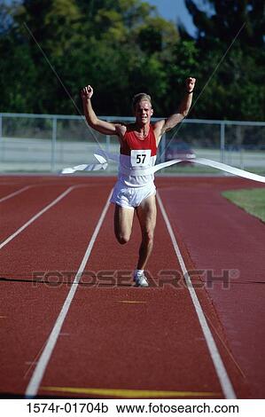 Stock Image - Portrait of a male runner crossing the finishing line with his arms raised. Fotosearch