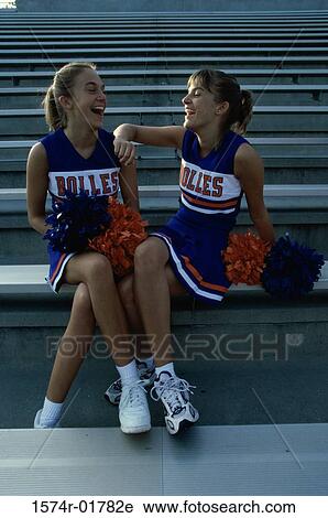 Stock Image - Two cheerleaders sitting with pom-poms. Fotosearch