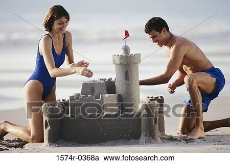 Stock Image - Couple building a sandcastle at the beach. Fotosearch