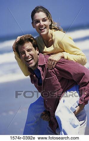Portrait of a young woman riding piggyback on a young man at the beach View Large Photo Image Stock Image - Portrait of a young woman riding piggyback on a young man at the beach. Fotosearch