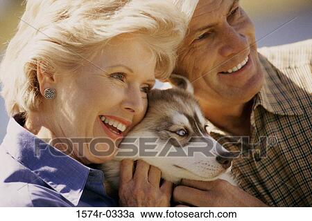 Senior couple sitting together holding a dog View Large Photo Image Stock Image - Senior couple sitting together holding a dog. Fotosearch