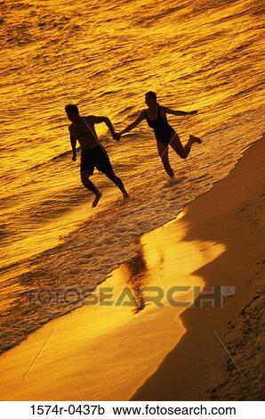 Silhouette of a young couple running at the beach holding hands View Large Photo Image Stock Image - Silhouette of a young couple running at the beach holding hands. Fotosearch