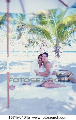 Young couple sitting together at the beach holding each other View Large Photo Image Stock Image - Young couple sitting together at the beach holding each other. Fotosearch