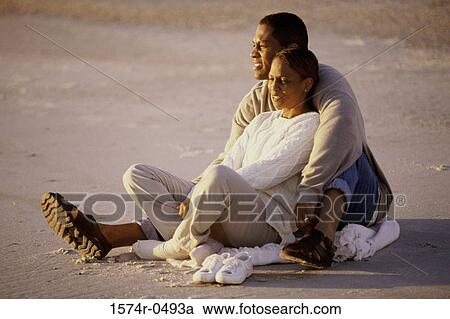 Stock Image - Young couple sitting together at the beach. Fotosearch