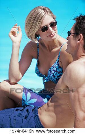 Stock Image - Young couple sitting together near a swimming pool. Fotosearch