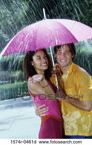Young couple standing under an umbrella in the rain View Large Photo Image Stock Image - Young couple standing under an umbrella in the rain. Fotosearch